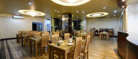 Un comedor espacioso con mesas y sillas de madera, iluminación empotrada y suelo pulido.