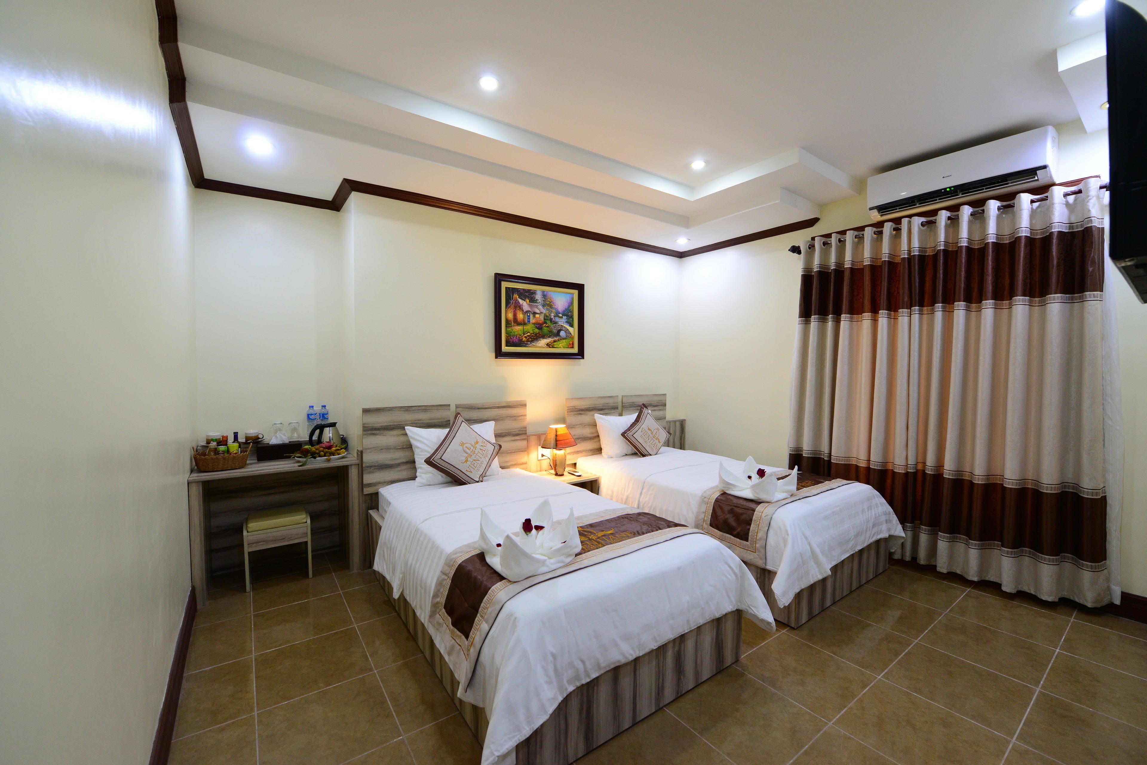 A hotel room with two beds, a nightstand with a lamp, a painting on the wall, and a window with curtains.