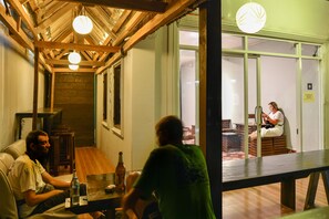 A room with a wooden ceiling, a table with bottles, and a person sitting at a desk. - Aham Backpackers Hostel - Adults Only (Luang Prabang)