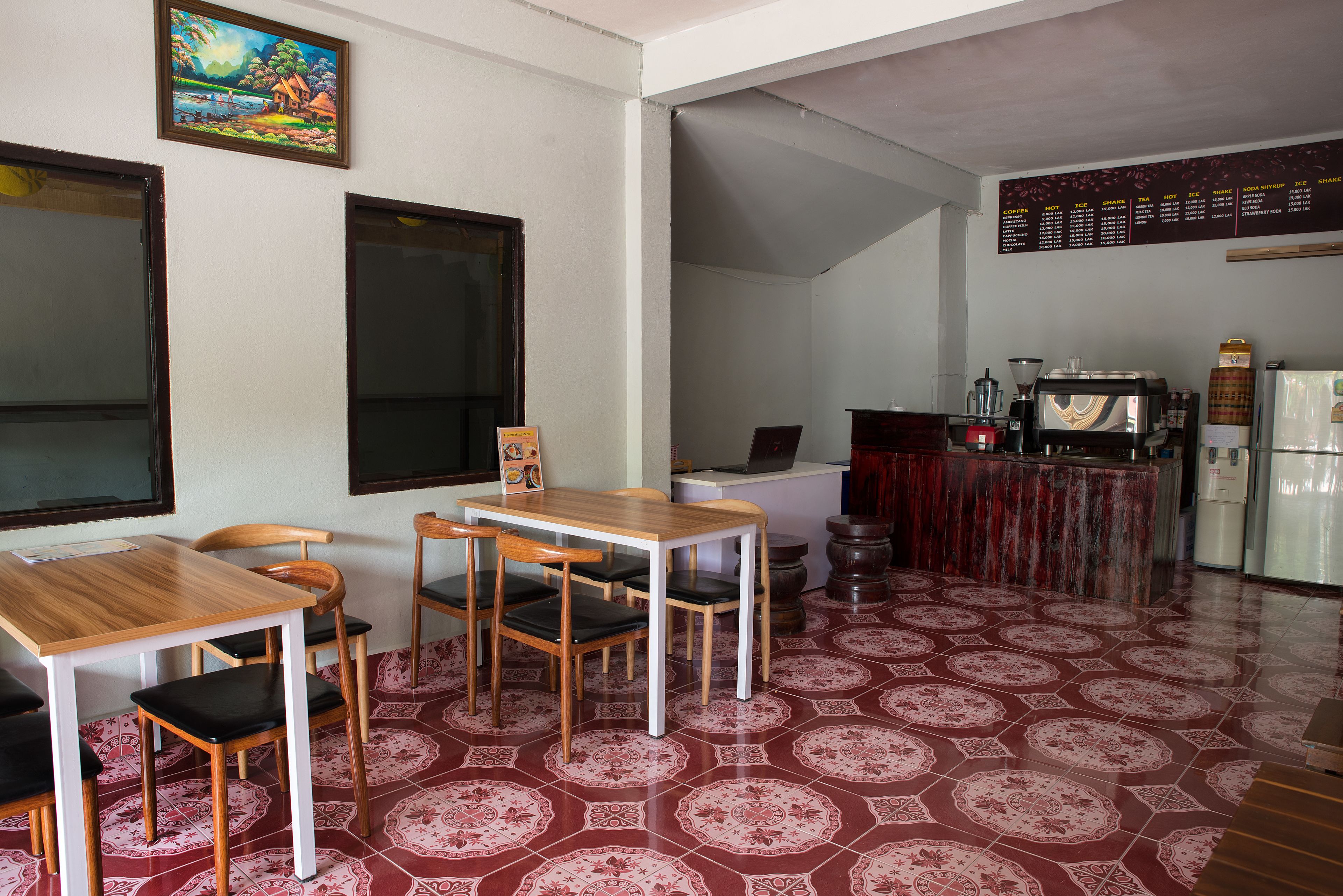Un coin repas avec une table et des chaises en bois, une cuisine équipée d’une machine à café et un sol à motifs.