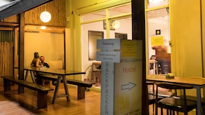Et hostel med træbænke og borde, et billetskilte og et hostel-skilt med kontaktoplysninger.