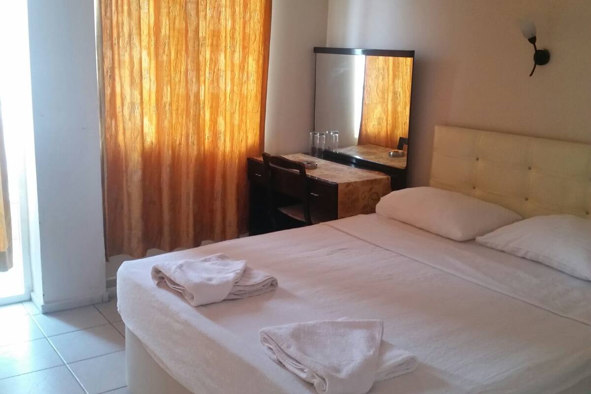 Een hotelkamer met een bed, een bureau, een stoel, een spiegel en een raam met gordijnen.
