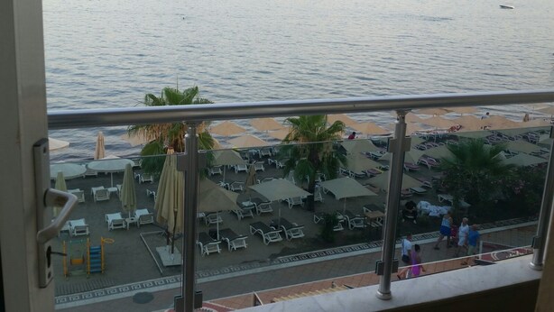 Un balcon avec vue sur une mer calme et des montagnes lointaines. Des chaises longues et des parasols sont disposés sur la terrasse.