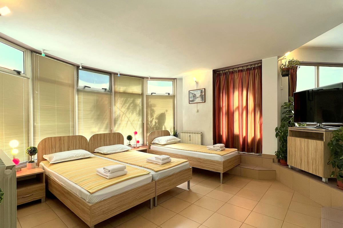 A hotel room with two beds, a TV, a desk, and a window with curtains.