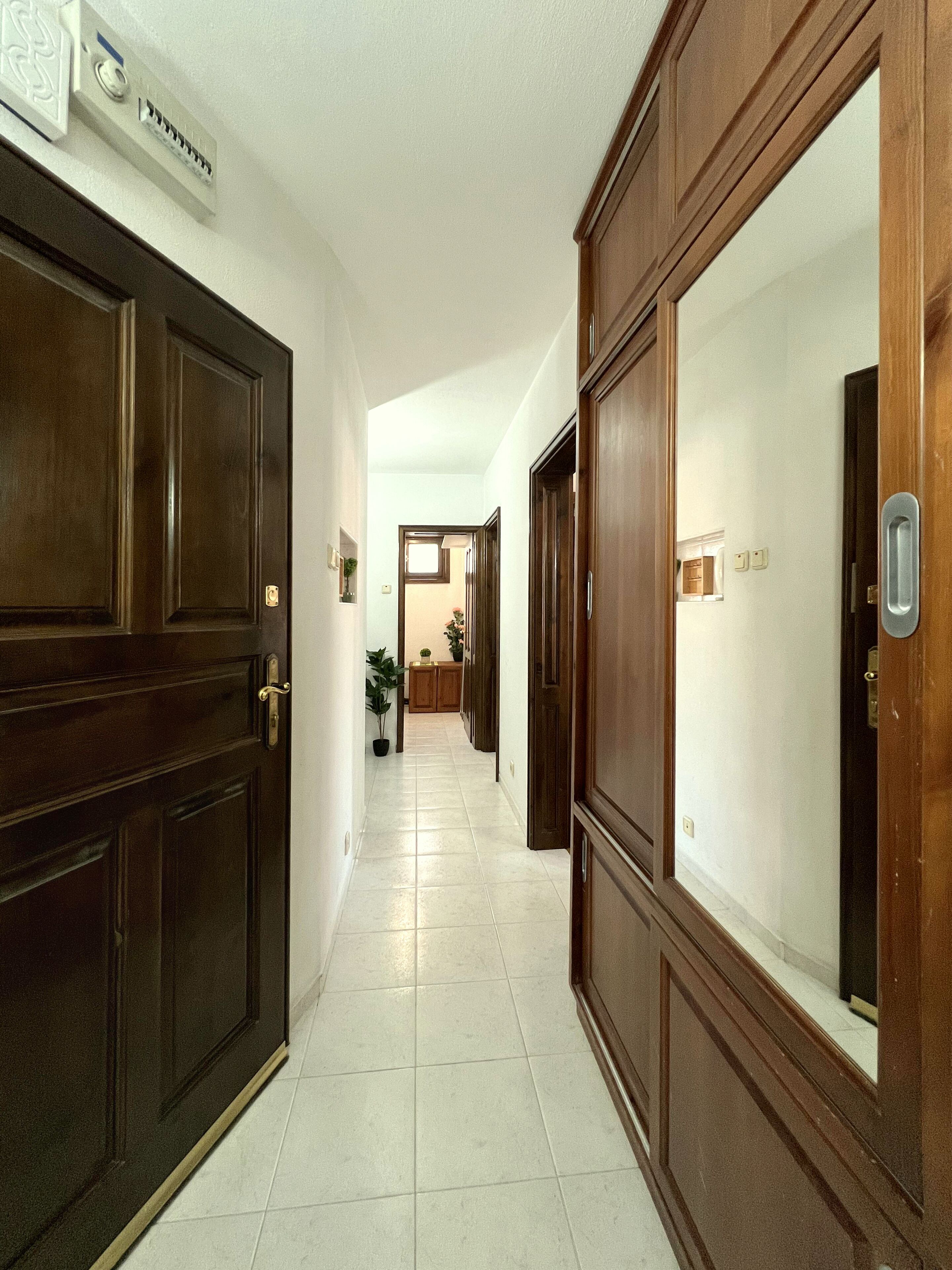 A hallway with wooden doors and white tiled flooring.