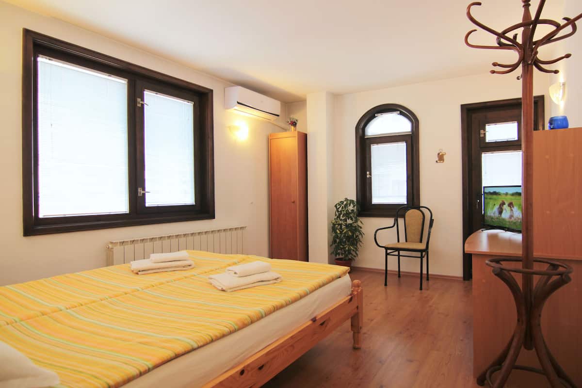 A bedroom with a bed, a chair, a TV, and a coat rack.