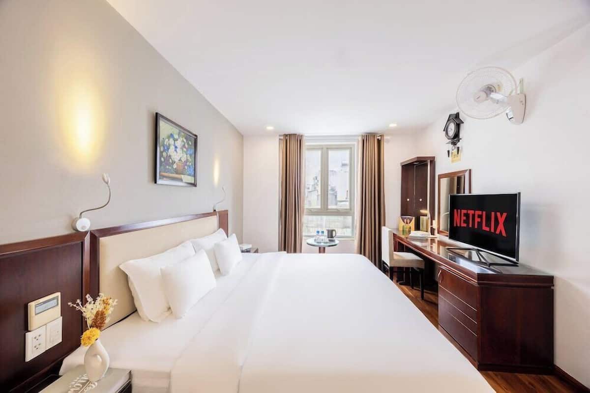 A hotel room with a bed, bedside table, TV, and a window with curtains.