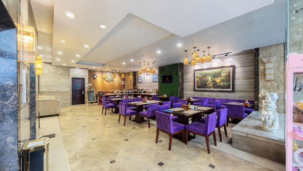 A spacious restaurant with purple chairs and tables, a green wall with a painting, and a marble floor. - A25 Premium Hotel - 180 Nguyen Trai (Ho Chi Minh City)