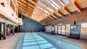 A modern indoor swimming pool with skylights, benches, and a clear view of the outside.