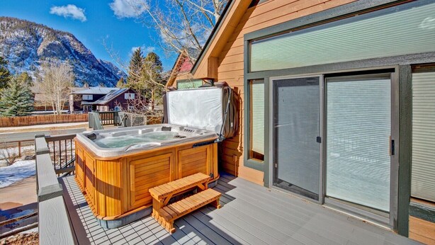 A wooden hot tub on a deck with a mountain view, a sliding glass door, and a wooden fence.