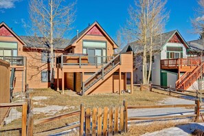Une rangée de cabanes en bois dotées de balcons et accessibles par des escaliers, entourées d’une clôture en bois et d’arbres.