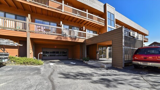 A multi-story building with a garage entrance, a covered outdoor area, and a red car parked in front. - Cedar Lodge  309 Studio Bedroom Condo by RedAwning (Frisco)