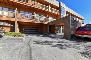 Un immeuble à plusieurs étages avec une entrée de garage, un espace extérieur couvert et une voiture rouge garée devant.