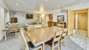 A dining area with a wooden table and chairs, a television mounted on the wall, and a kitchen area with wooden cabinets and a tiled backsplash. - Cedar Lodge  309 Studio Bedroom Condo by RedAwning (Frisco)