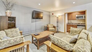 A living room with a sofa set, a coffee table, a TV mounted on the wall, and a kitchen area with wooden cabinets and a microwave. - Cedar Lodge  309 Studio Bedroom Condo by RedAwning (Frisco)