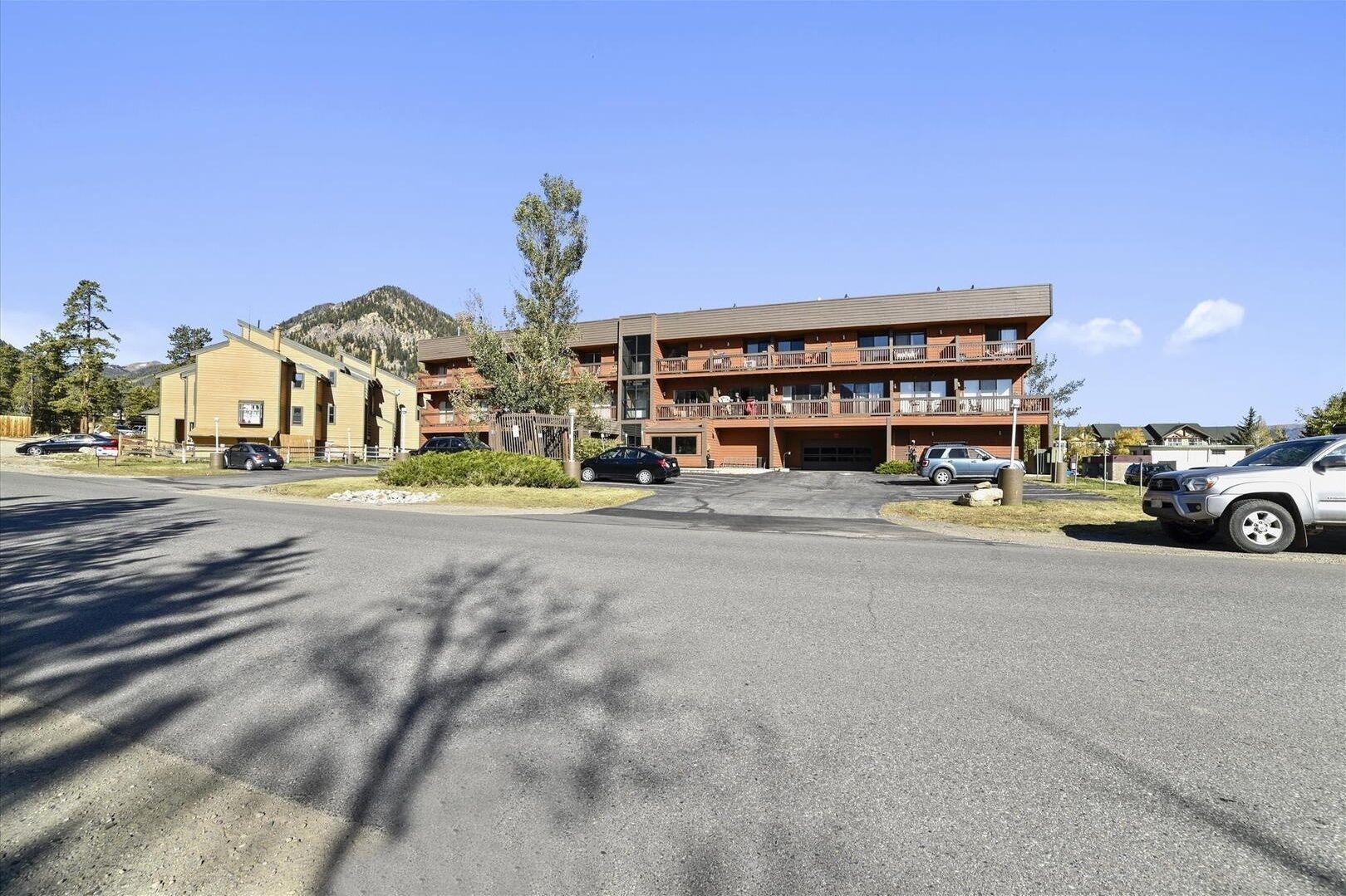 A multi-story hotel with a flat roof and balconies, surrounded by a parking lot and trees.