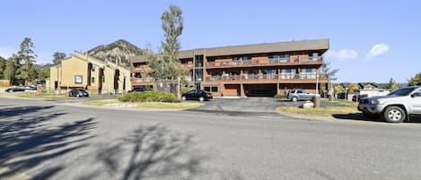 A multi-story hotel with a flat roof and balconies, surrounded by a parking lot and trees.