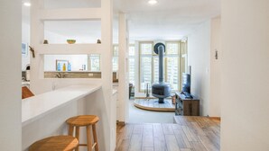 Una cocina moderna con una isla central, taburetes de madera, estufa empotrada y vistas al salón a través de amplias ventanas.
