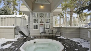 Un jacuzzi en un espacio exterior cubierto con terraza de madera, rodeado por una valla blanca y árboles.