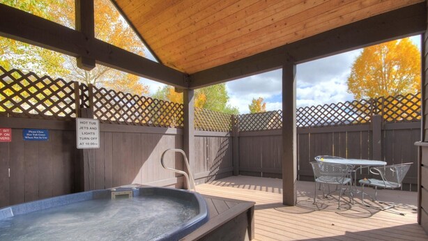 A covered outdoor hot tub area with a wooden deck, metal chairs, and a table. - Tarn Landing  #c-4 2 Bedroom Condo by RedAwning (Frisco)