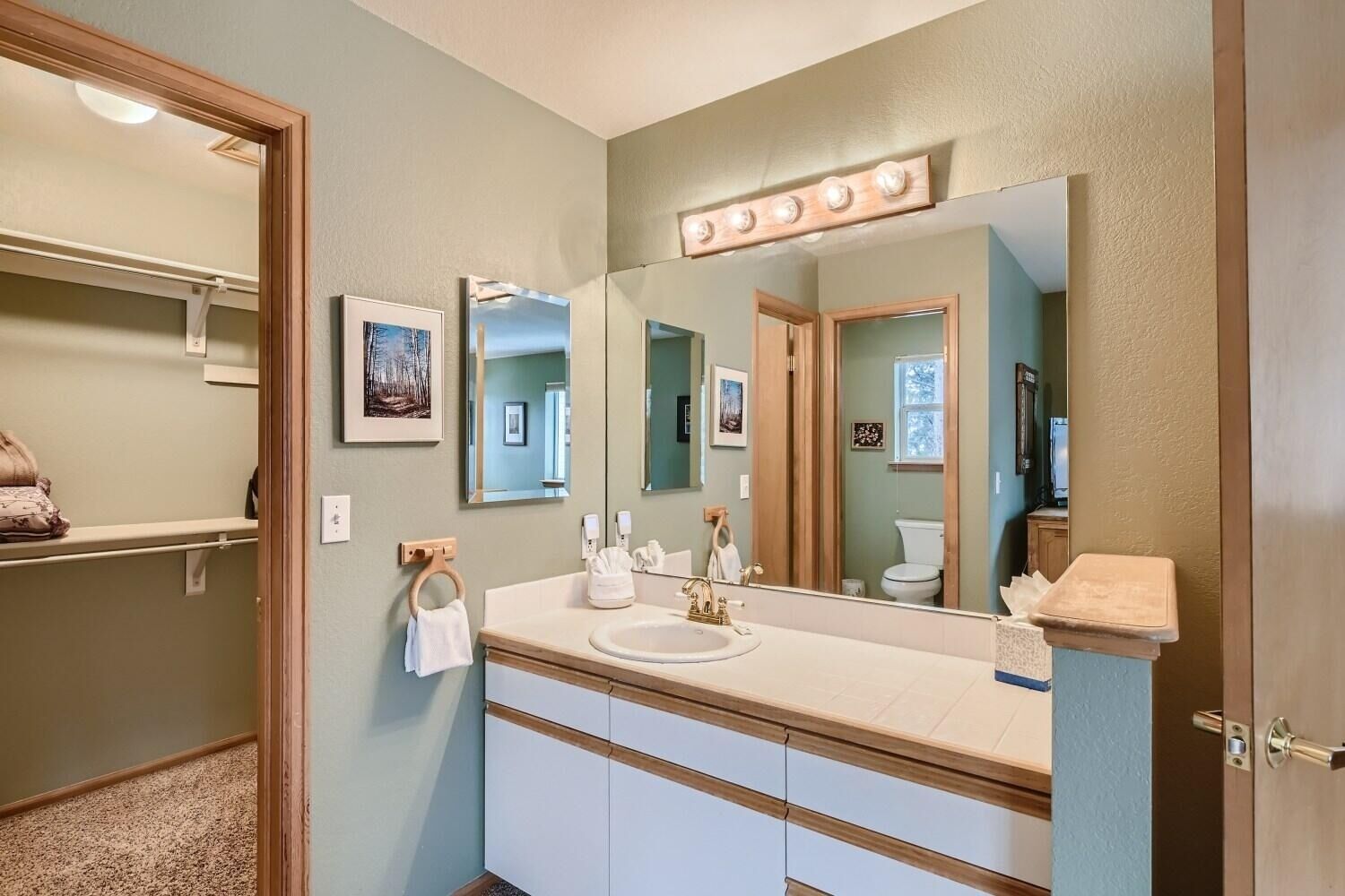 A bathroom with a large mirror, vanity with a sink, and a towel rack.