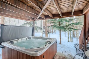 A hot tub in a wooden cabin with a view of snow-covered ground and trees.