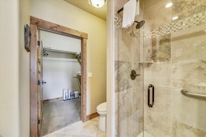 A bathroom with a glass shower enclosure, a wooden door frame, and a visible toilet.