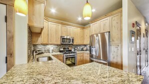 A kitchen with wooden cabinets, stainless steel appliances, granite countertops, and pendant lighting. - S Off Main  #4 2 Bedroom Condo by RedAwning (Frisco)