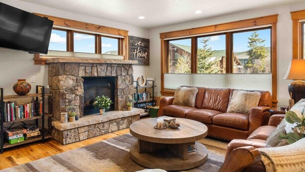 A cozy living room with a stone fireplace, leather sofa, and large windows offering a mountain view. - Mount Victoria Lodge #d 3 Bedroom Condo by RedAwning (Frisco)