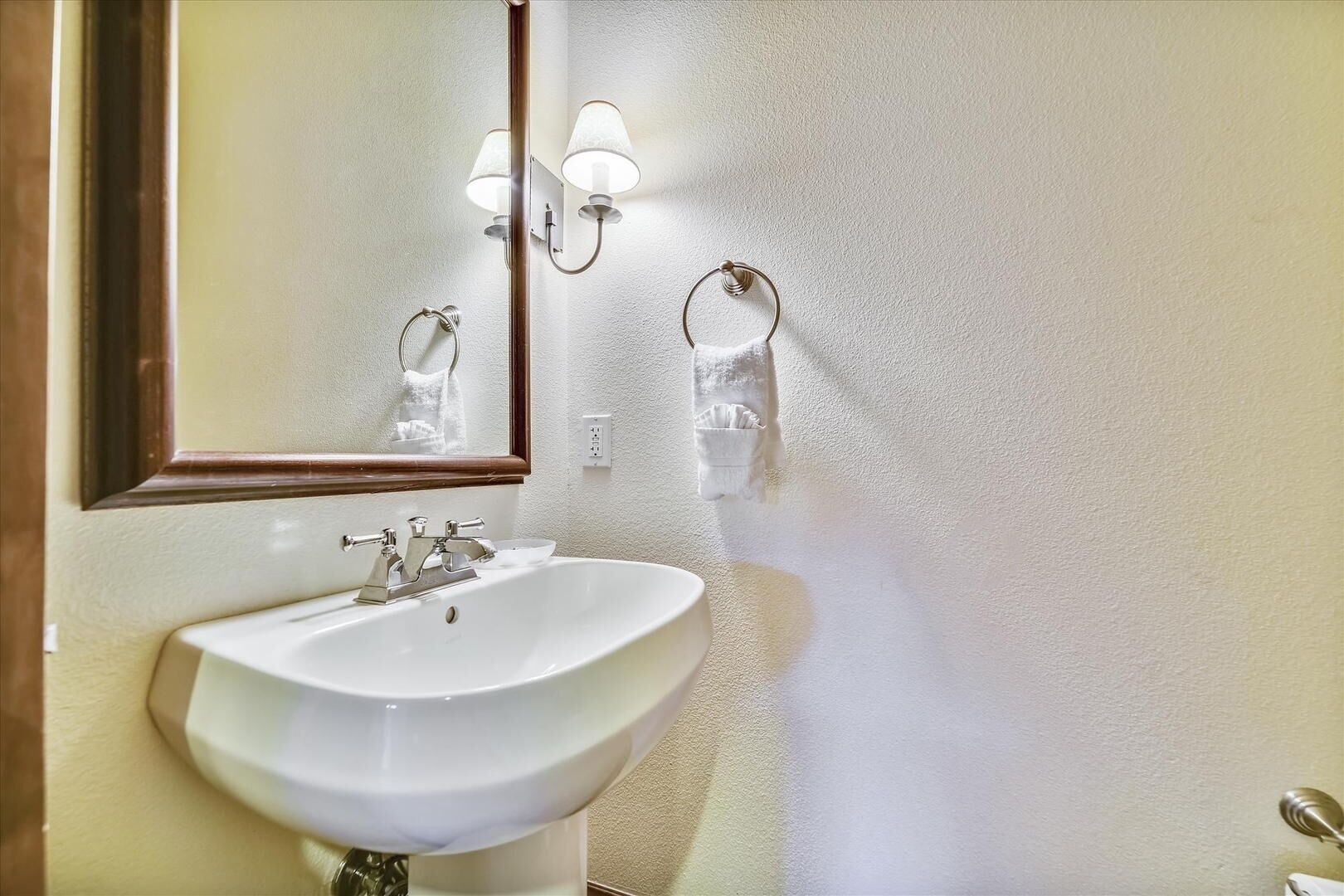 Une salle de bain avec un lavabo blanc, un miroir et deux appliques murales.
