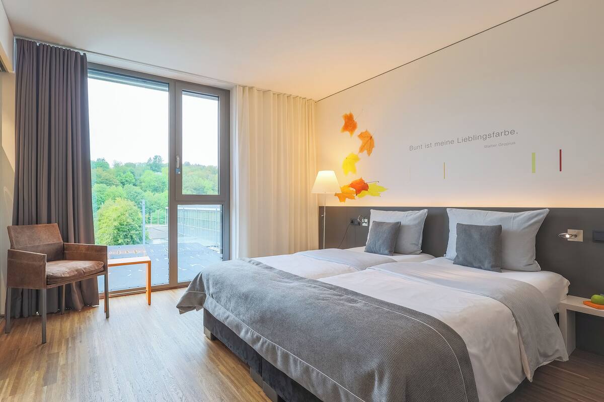 A modern hotel room with a large bed, a chair, and a view of the outdoors.