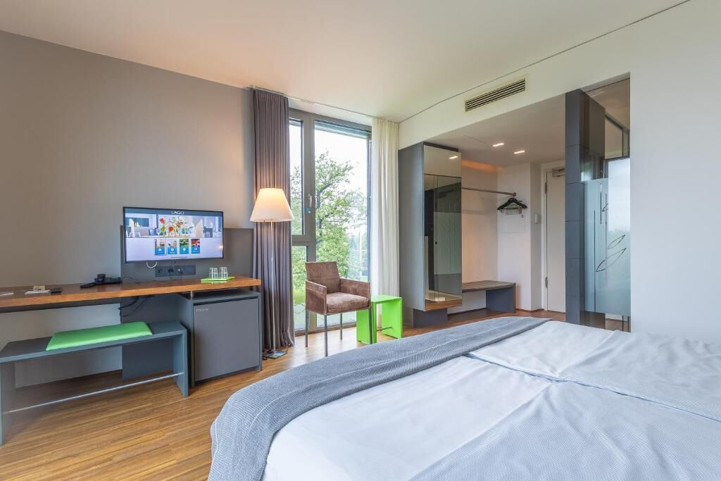 A modern hotel room with a bed, desk, chair, and a TV.