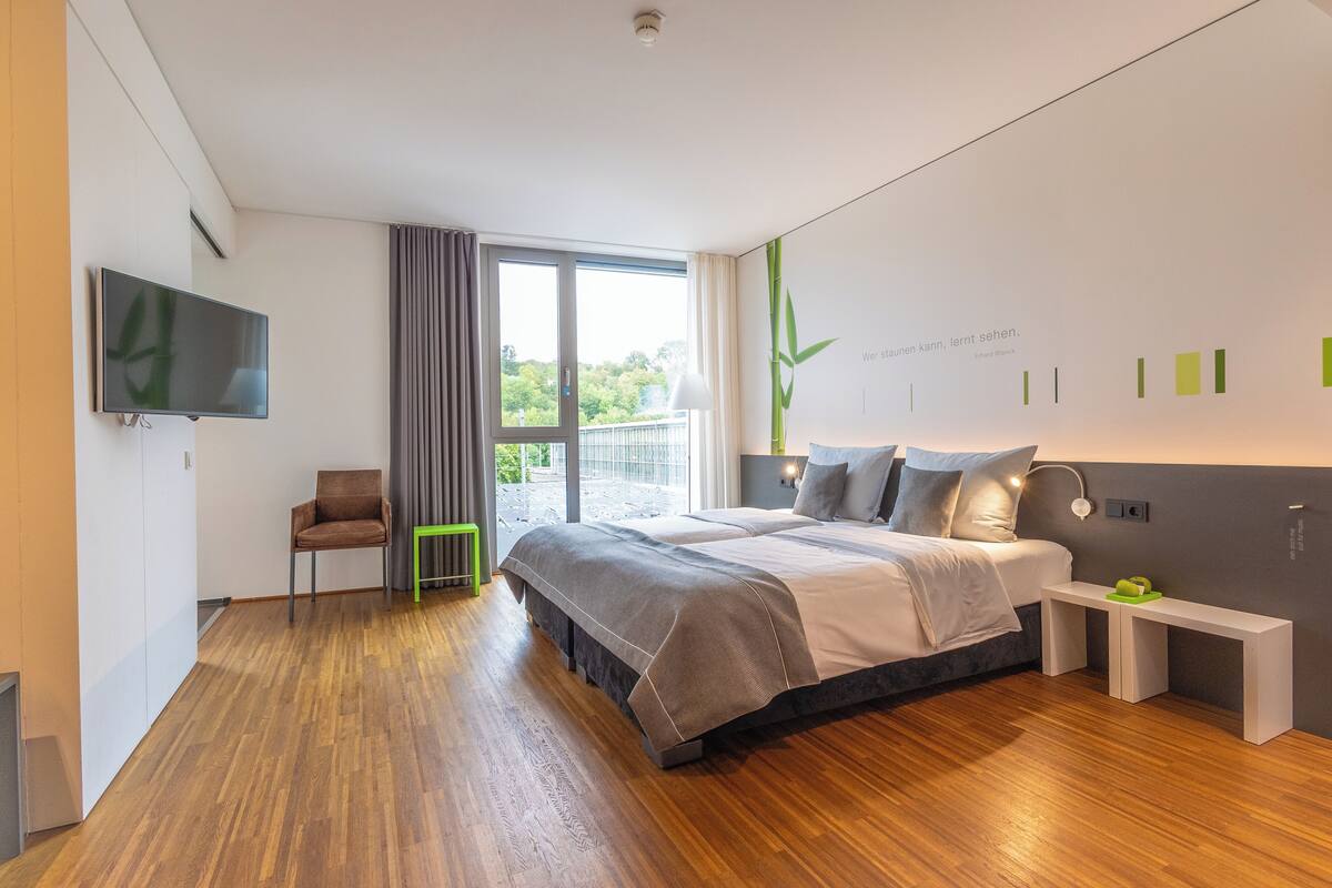 A modern bedroom with a large bed, a TV mounted on the wall, a chair, and a bench.