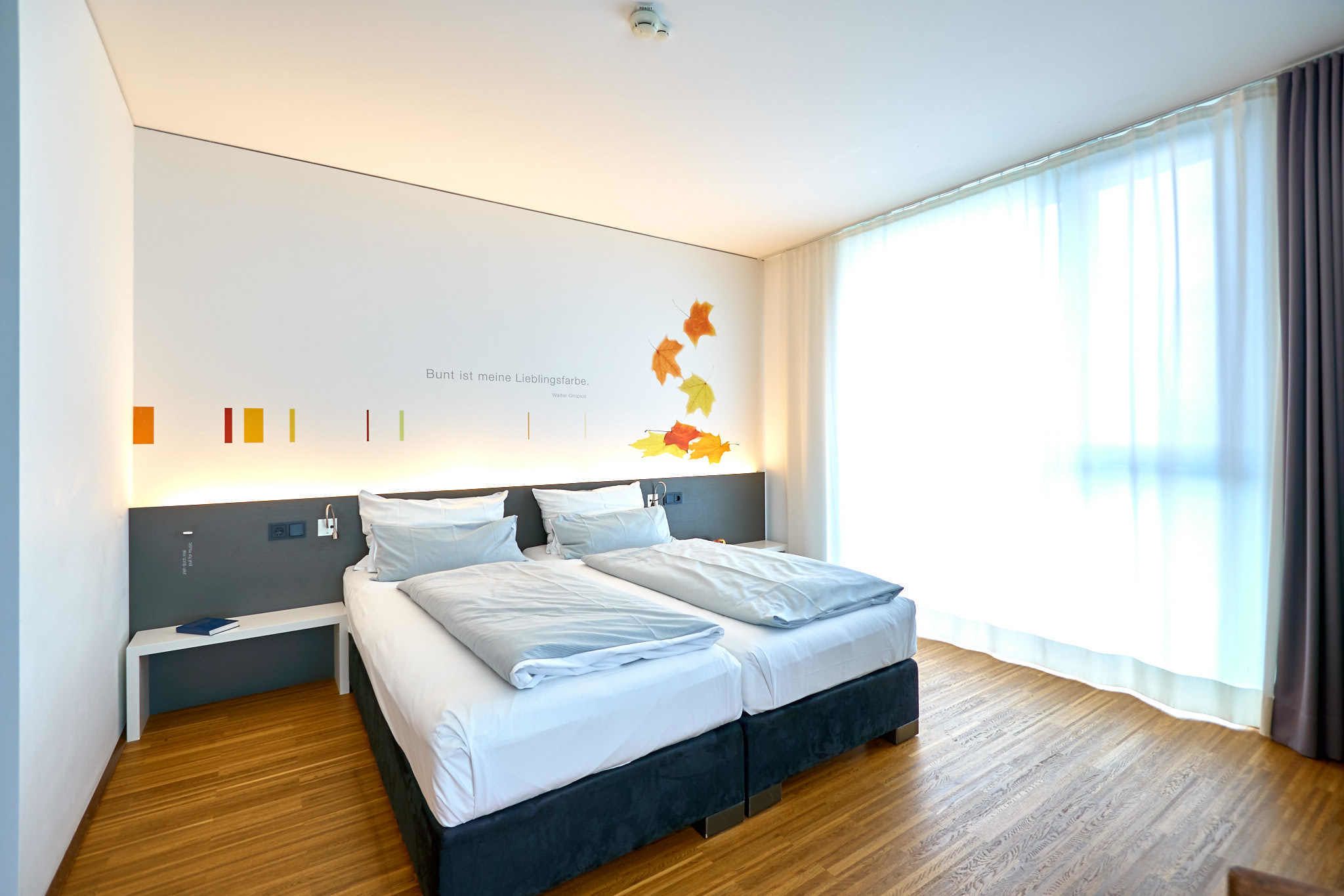 Quarto de hotel moderno com uma cama grande, uma mesa de cabeceira e vista para o exterior.