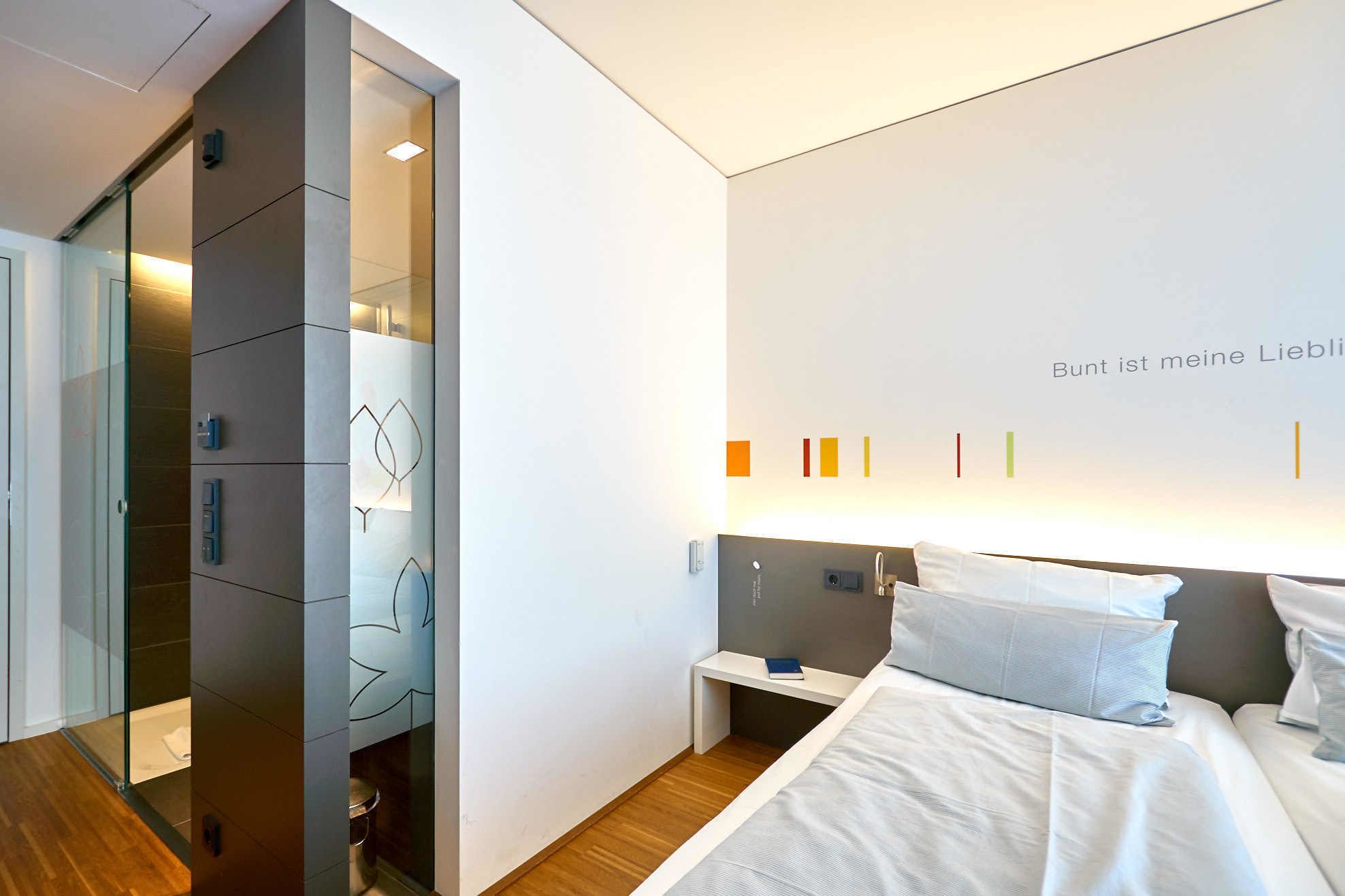 A modern bedroom with a bed, bedside table, and a wall with a light fixture and a text.