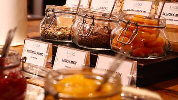 Variedad de alimentos en frascos de vidrio con etiquetas, como nueces, semillas y frutas deshidratadas.