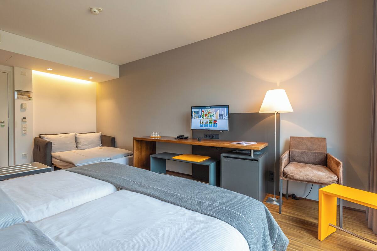 A modern hotel room with two beds, a desk with a computer, a chair, and a lamp.