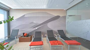 Relax in a serene spa room with a stunning wall mural, comfortable lounge chairs, and a wooden bench.