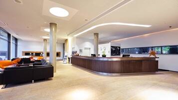 A modern reception area with a curved reception desk, seating area with orange chairs, and large windows providing views of the outside.