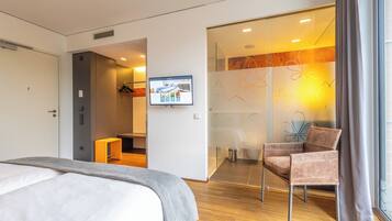 Una habitación de hotel moderna con una cama, un televisor montado en la pared, una silla y un separador de vidrio con un diseño floral.