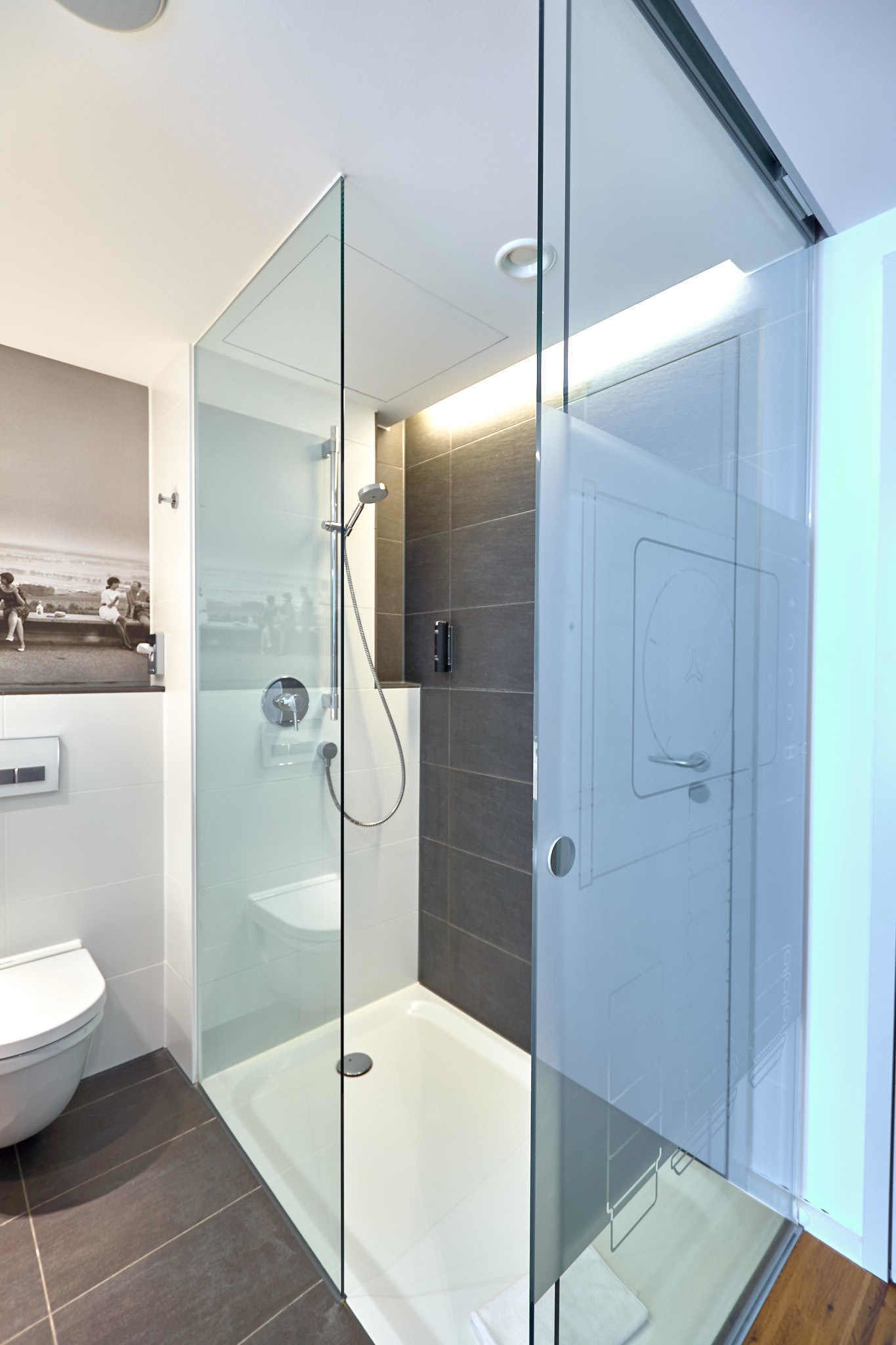 Ein modernes Badezimmer mit einer gläsernen Duschkabine, einer weißen Toilette und Fliesenboden.