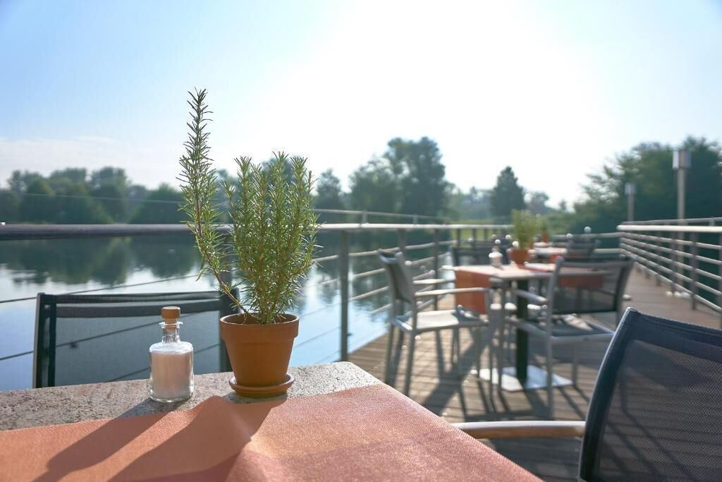 A deck with outdoor seating overlooking a body of water, featuring a potted plant and a salt shaker.