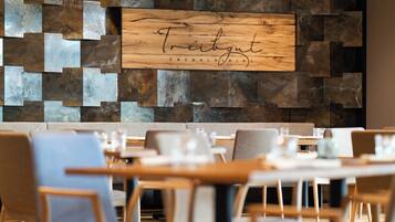 A restaurant interior with a wooden sign reading "Treibgut Casual Dining" and a modern, geometric wall design. Tables and chairs are arranged for dining.
