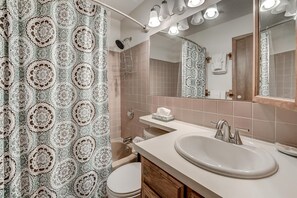 A bathroom with a patterned shower curtain, a bathtub, a sink with a mirror, and a toilet.