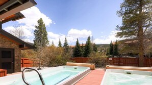 A hot tub area with two hot tubs, a wooden deck, and a stone building. - Mountainside 229e 1 Bedroom Condo by RedAwning (Frisco)