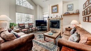 Un salón amplio con sofás de cuero, una chimenea, televisión y ventanas grandes.