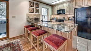 Una cocina moderna con encimera de granito, armarios de madera, refrigerador de acero inoxidable y un ventanal grande.