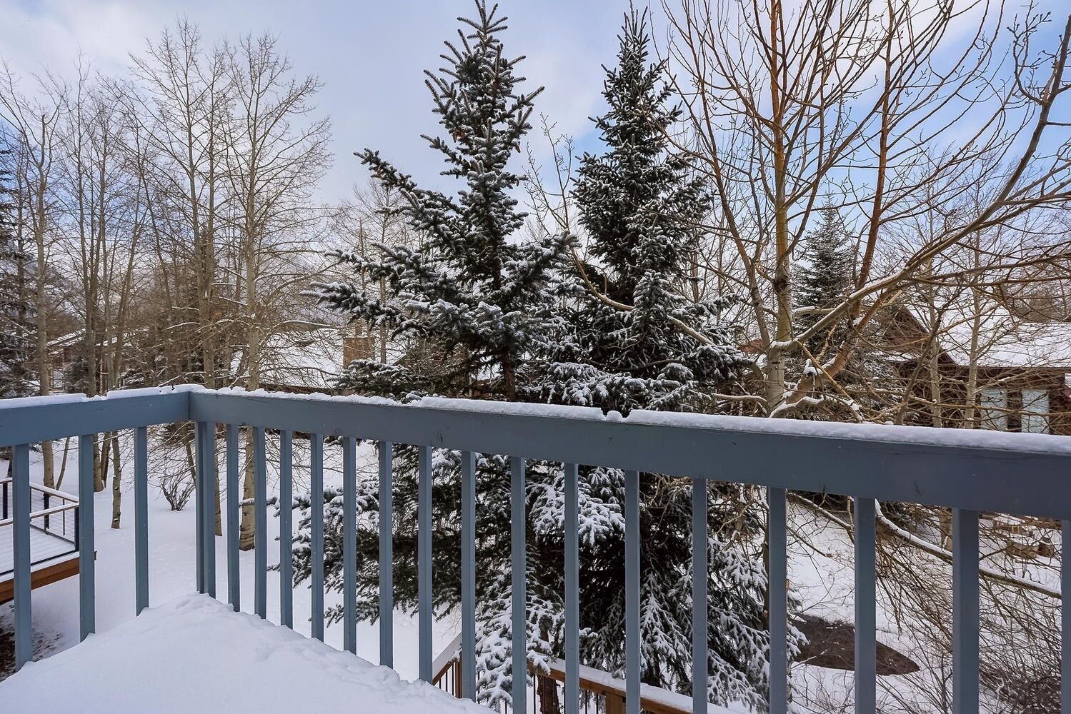 Un muelle cubierto de nieve con barandilla, rodeado de árboles y una casa al fondo.