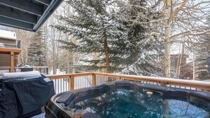 Un jacuzzi en una terraza de madera, con árboles nevados al fondo.