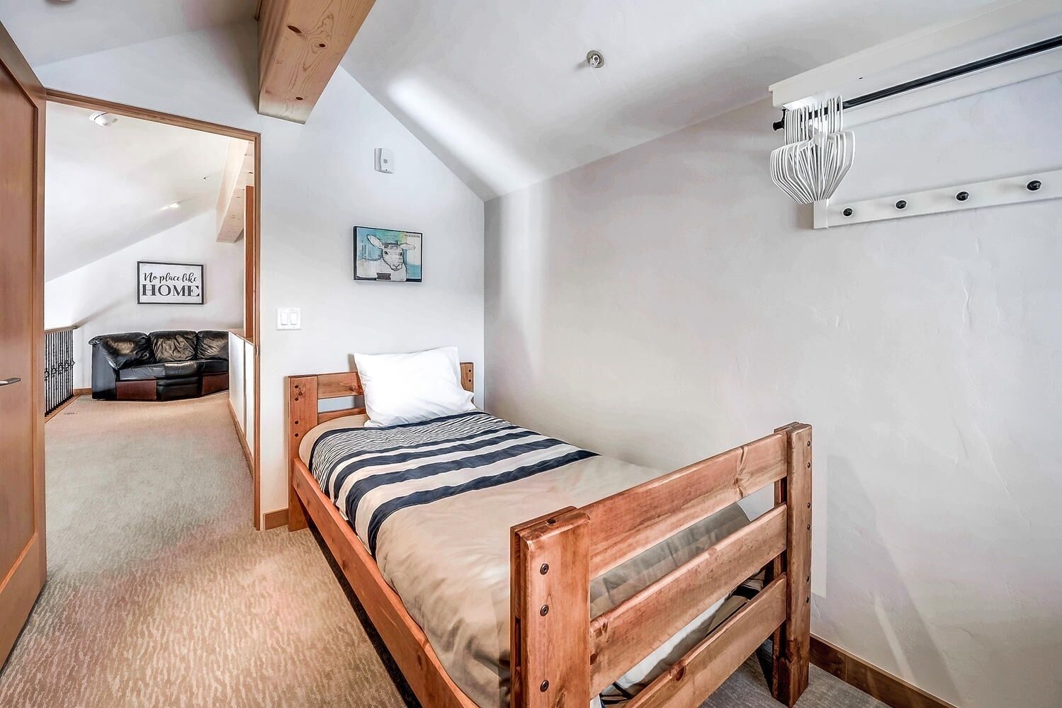 A bedroom with a wooden bed, a black leather sofa, a framed picture on the wall, and a ceiling fan.